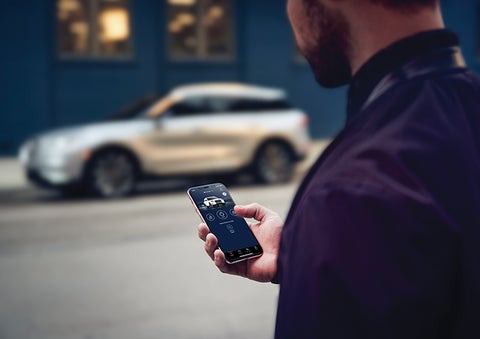 A person is shown interacting with a smartphone to connect to a Lincoln vehicle across the street. | Thomasville Lincoln in Thomasville GA